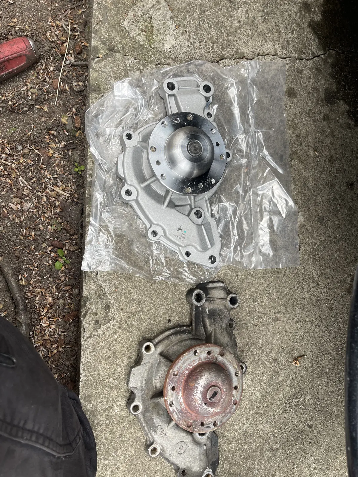 Old Holden VX water pump beside its new replacement before installation