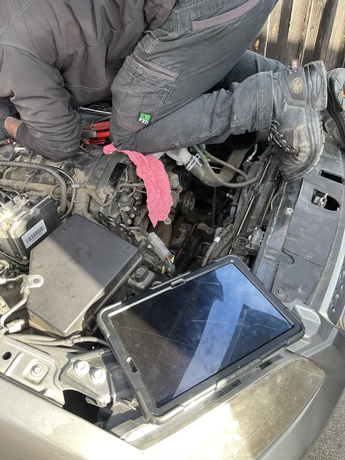 Mechanic working in the engine bay with a diagnostic tablet nearby