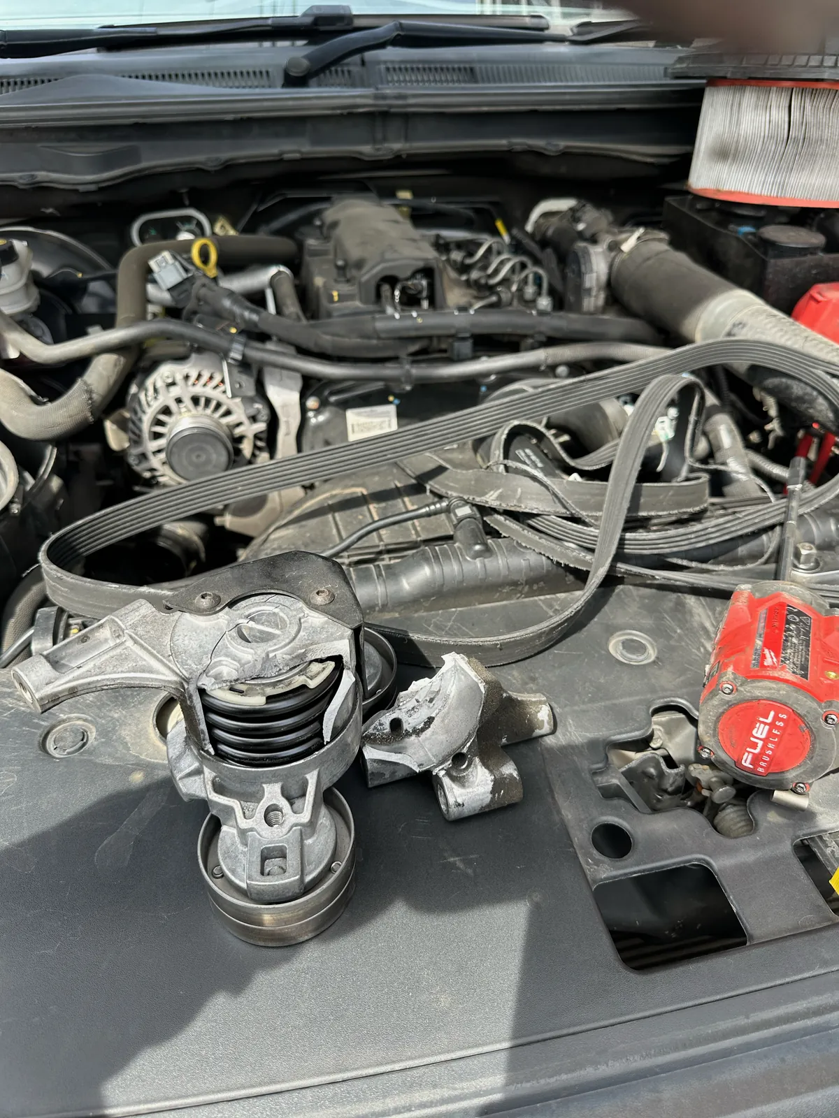 Broken Ford Ranger tensioner and separated fragment beside the damaged drive belt