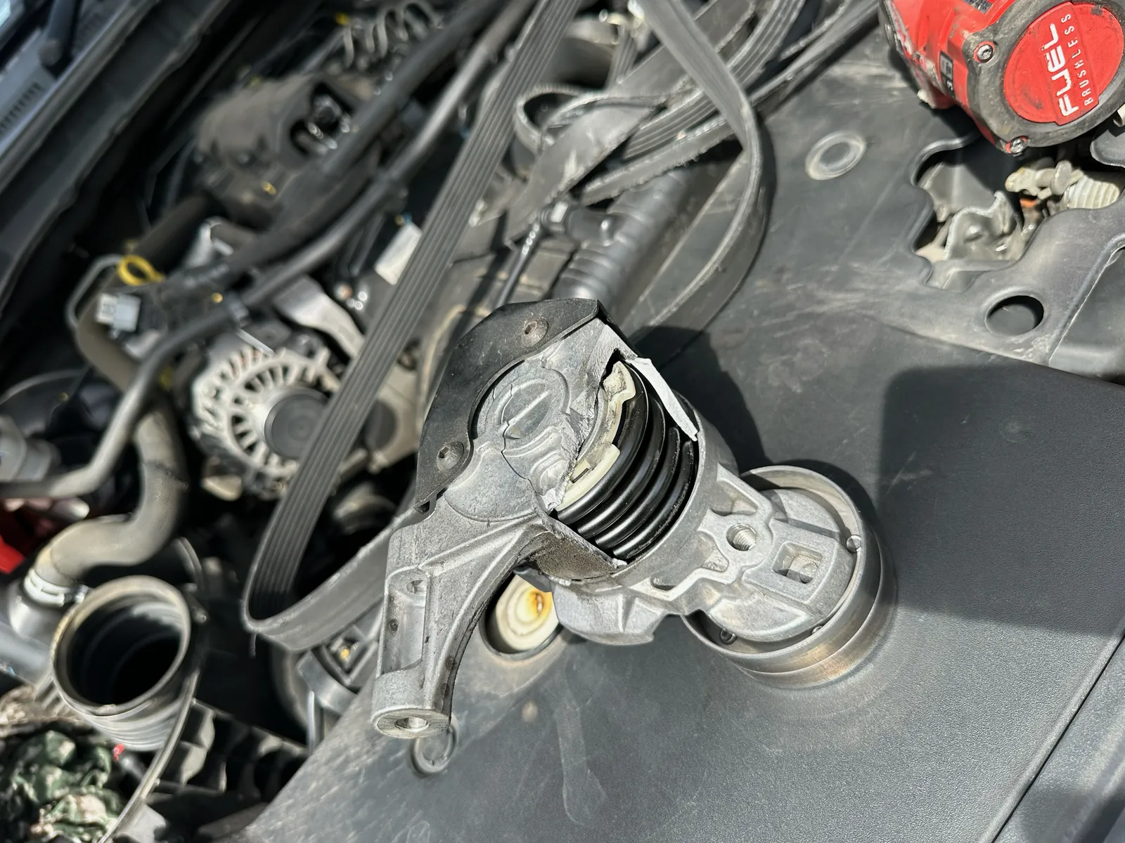 Removed Ford Ranger tensioner with its spring exposed beside the shredded belt